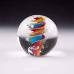 Handcrafted Eternity Sphere memorial made with cremation ash, featuring a flowing multicolor spiral of teal, amber, and pink encased in clear glass with fine ash inclusions throughout.