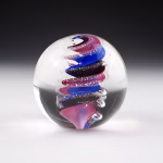 Handcrafted Eternity Sphere memorial made with cremation ash, featuring a flowing blue and pink spiral suspended in clear glass with fine ash inclusions throughout the design.