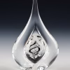 Teardrop memorial glass keepsake with cremation ash, featuring a clear sculpted teardrop shape and a black spiral design suspended within the inner glass chamber, photographed upright against a dark studio background.