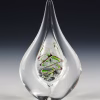 Teardrop memorial glass keepsake containing cremation ash, with a clear sculpted teardrop form and a green and purple spiral design suspended inside the glass, photographed upright against a dark studio background.