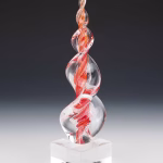 Red and orange Legacy Flame cremation ash sculpture featuring hand-blown clear glass with vibrant swirling red-orange accents, crafted as an elegant memorial art glass keepsake displayed on a polished glass base.