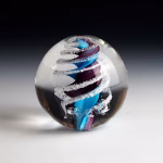 Handcrafted Eternity Sphere memorial made with cremation ash, featuring a flowing blue and violet spiral encased in clear glass with fine ash inclusions suspended along the curved form.