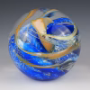 Ocean Memorial Cremation Paperweight in blue and gold, featuring a hand-blown glass sphere with deep ocean blues, soft white highlights, and flowing golden ribbons suspended within the glass.