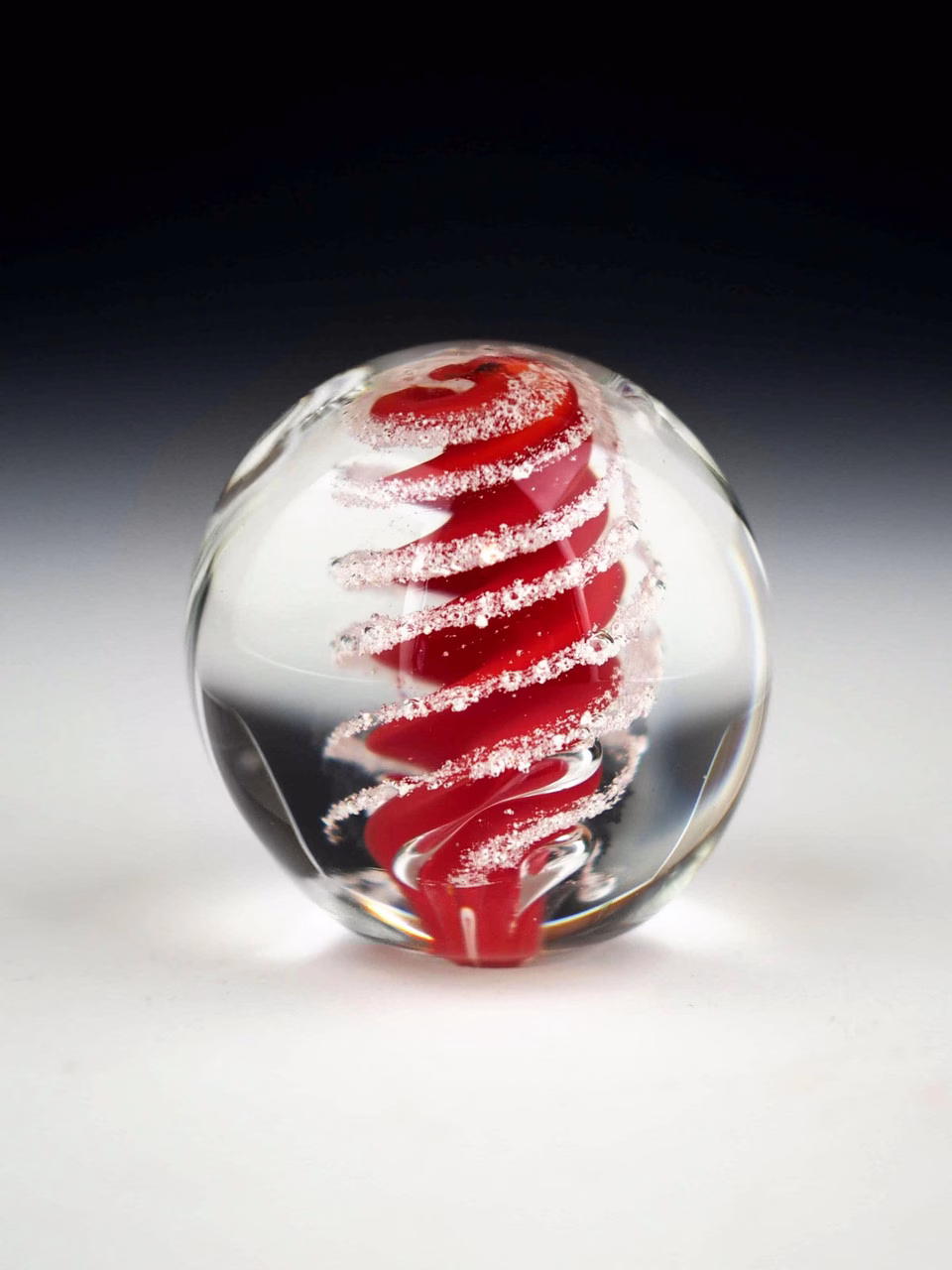 Handcrafted Eternity Sphere memorial made with cremation ash, featuring a rich red spiral suspended in clear glass with fine ash inclusions following the flowing spiral form.