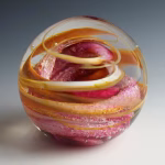 Ocean Memorial Cremation Paperweight in pink and gold, featuring a hand-blown glass sphere with soft rose tones, warm golden ribbons, and flowing layered movement captured within the glass.