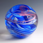 Ocean Memorial Cremation Paperweight featuring a hand-blown glass sphere with rich blue tones and flowing ribbon-like swirls, accented with soft pink highlights and subtle internal texture.