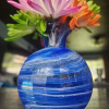 Round vase memorial with cremation ashes in layered blue glass holding colorful flowers