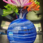 Round vase memorial with cremation ashes in layered blue glass holding colorful flowers