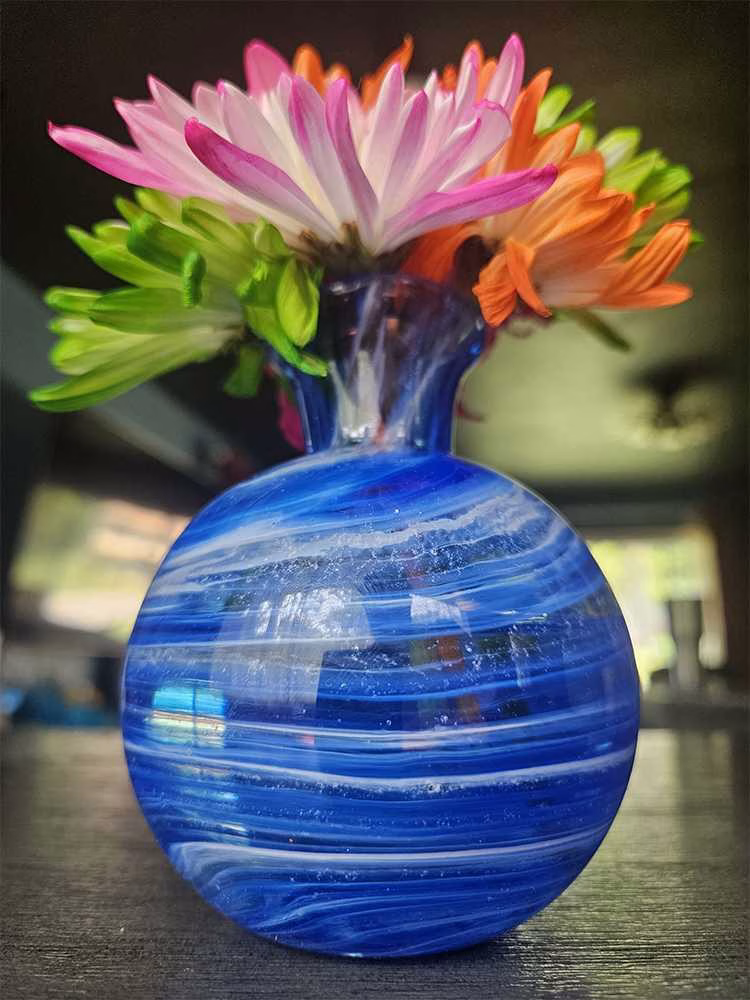 Round vase memorial with cremation ashes in layered blue glass holding colorful flowers