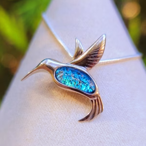 Front-facing view of a hummingbird cremation pendant with sculpted silver wings and a vibrant blue memorial inlay, displayed on a necklace against a soft neutral background.