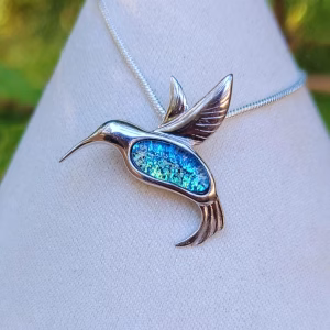 Hummingbird cremation pendant featuring a silver bird design with an iridescent blue memorial inlay, displayed on a necklace against a neutral background.