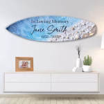 Oceanside Memorial Surfboard with cremation ash, featuring ocean blue and white wave design with seashell details and personalized memorial text, displayed horizontally mounted on a living room wall above a modern console