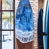 Oceanside memorial surfboard with cremation ash featuring layered ocean waves in blue and white resin displayed upright against a brick wall beside other surfboards