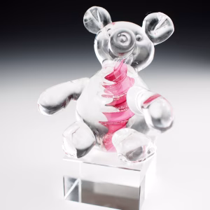 A clear glass teddy bear sculpture displayed on a transparent square base, featuring a pink swirling core that contains incorporated cremation ash.