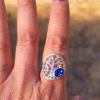 Family Tree cremation ring worn on a finger, featuring a silver tree design with a round sparkling blue memorial glass stone containing cremation ash.