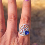 Family Tree cremation ring worn on a finger, featuring a silver tree design with a round sparkling blue memorial glass stone containing cremation ash.