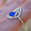 Side view of a Family Tree cremation ring worn on a finger, showing the silver tree design and a round sparkling blue memorial glass stone containing cremation ash.
