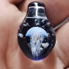 Handcrafted dark blue glass cremation pendant featuring an intricate white jellyfish suspended inside alongside scattered white flecks of encased cremation ashes, shown resting in the hand for a close-up view of detail, depth, and color