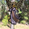 Guardian Angel suncatcher made with cremation ash, featuring soft earth-toned stained glass robes, detailed angel wings, and a hanging crystal accent, illuminated by natural light against a wooded backdrop.