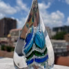 Pyramid Memorial with Cremation Ash in aqua, blue, and green glass displayed outdoors with city background