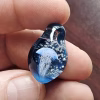 Handcrafted glass jellyfish cremation pendant held between fingers, featuring a detailed white jellyfish suspended in deep blue glass with swirling white flecks of encased cremation ashes, shown in a close-up to highlight color and intricate design
