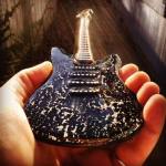 Close-up of a memorial glass guitar made with cremation ash, held in hand with dark glass body and ash inclusions catching the light.