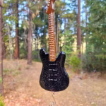 Hanging memorial guitar suncatcher made with cremation ash, black glass guitar suspended outdoors with crystal accent.
