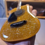 Close-up of a golden glass memorial guitar incorporating cremation ash, showing textured details and strings while held in hand.