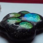 Close-up of a handcrafted paw print cremation stone made with cremation ash, showing a glossy black memorial glass surface with iridescent paw pad details and fine ash inclusions.