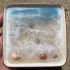 Oceanside Ring Dish with Cremation Ash in a square ceramic dish featuring an ocean wave design, sandy shoreline, and embedded seashells