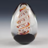 Handcrafted spiral egg-shaped cremation glass keepsake featuring a clear glass form with a warm red and orange spiral design and suspended cremation ashes inside.