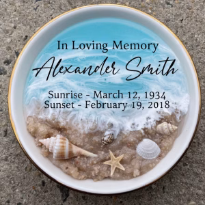 Oceanside Ring Dish with Cremation Ash in a round ceramic dish featuring ocean waves, sandy shoreline, seashells, a starfish, and personalized memorial text with name and dates