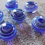 Group of handcrafted blue memorial prayer stones made with cremation ash, each featuring layered glass patterns and a smooth, rounded form designed to fit comfortably in the hand.