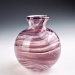 Round purple glass memorial vase with cremation ash visible inside swirling glass.