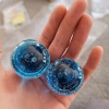 Two handcrafted blue memorial prayer stones made with cremation ash, viewed from the top and resting in the palm of a hand, showing layered glass swirls and delicate ash inclusions.