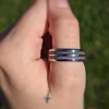 Dual Channel Cremation Ring with purple memorial inlay, worn on a hand outdoors in a side profile view