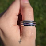 Dual Channel Cremation Ring with purple memorial inlay, worn on a hand outdoors in a side profile view