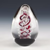 Handcrafted spiral egg-shaped cremation glass keepsake featuring a clear form with a red spiral design and suspended cremation ashes inside.