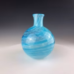 Round aqua glass memorial vase with cremation ash visible inside swirling glass.
