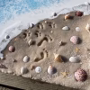 Close-up of an Oceanside Memorial made with cremation ash, featuring gentle wave details, seashells, starfish, and subtle footprints pressed into sand, evoking a peaceful shoreline remembrance.