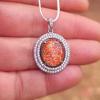 Halo Cremation Pendant with Cubic Zirconia in sterling silver, featuring a red orange memorial ash inlay displayed on a silver chain resting on a hand