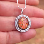 Halo Cremation Pendant with Cubic Zirconia in sterling silver, featuring a red orange memorial ash inlay displayed on a silver chain resting on a hand