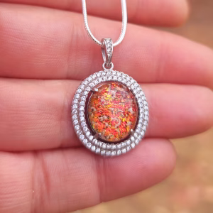Halo Cremation Pendant with Cubic Zirconia in sterling silver, featuring a red orange memorial ash inlay displayed on a silver chain resting on a hand
