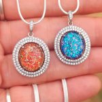 Halo Cremation Pendant with Cubic Zirconia in sterling silver, shown in blue and red orange memorial ash inlays on silver chains displayed side by side on a hand