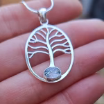 Close-up of the Family Tree Cremation Pendant in sterling silver, featuring a tree of life memorial design with a clear cremation ash glass cabochon held in a hand for scale