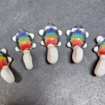 Five small glass turtle pendants arranged in a row on a work surface, each featuring a rainbow-colored shell with cremation ash suspended inside and white glass limbs and tail.