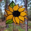 Sunflower suncatcher with bright yellow petals, green leaves, and a black center, handcrafted with cremation ash and hanging outdoors with crystal teardrop accents.