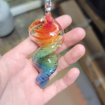 A single 3-inch rainbow glass spinner infused with cremation ash, featuring swirling red, orange, yellow, green, and blue colors, shown resting in a person's hand.