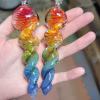 Two hand-blown 6-inch rainbow glass spinners infused with cremation ash, featuring swirling gradients of red, orange, yellow, green, and blue, shown resting in a person's hand.