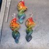 Three 3-inch rainbow glass spinner ornaments infused with cremation ash, arranged side by side on a workbench with swirling red, orange, yellow, green, and blue colors